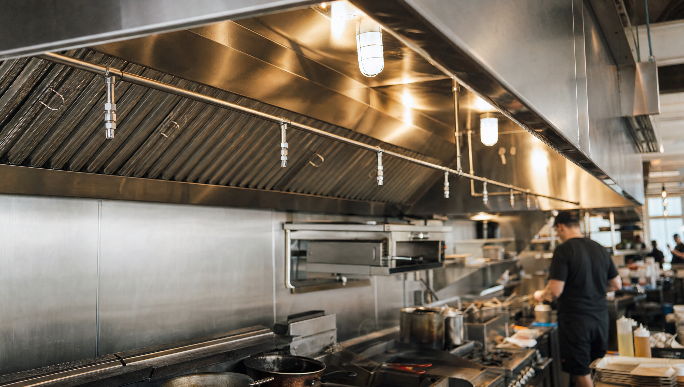 A stainless steel commercial kitchen exhaust hood with wet-chemical fire suppression nozzles above a cooking line in a busy Boulder, Colorado restaurant.